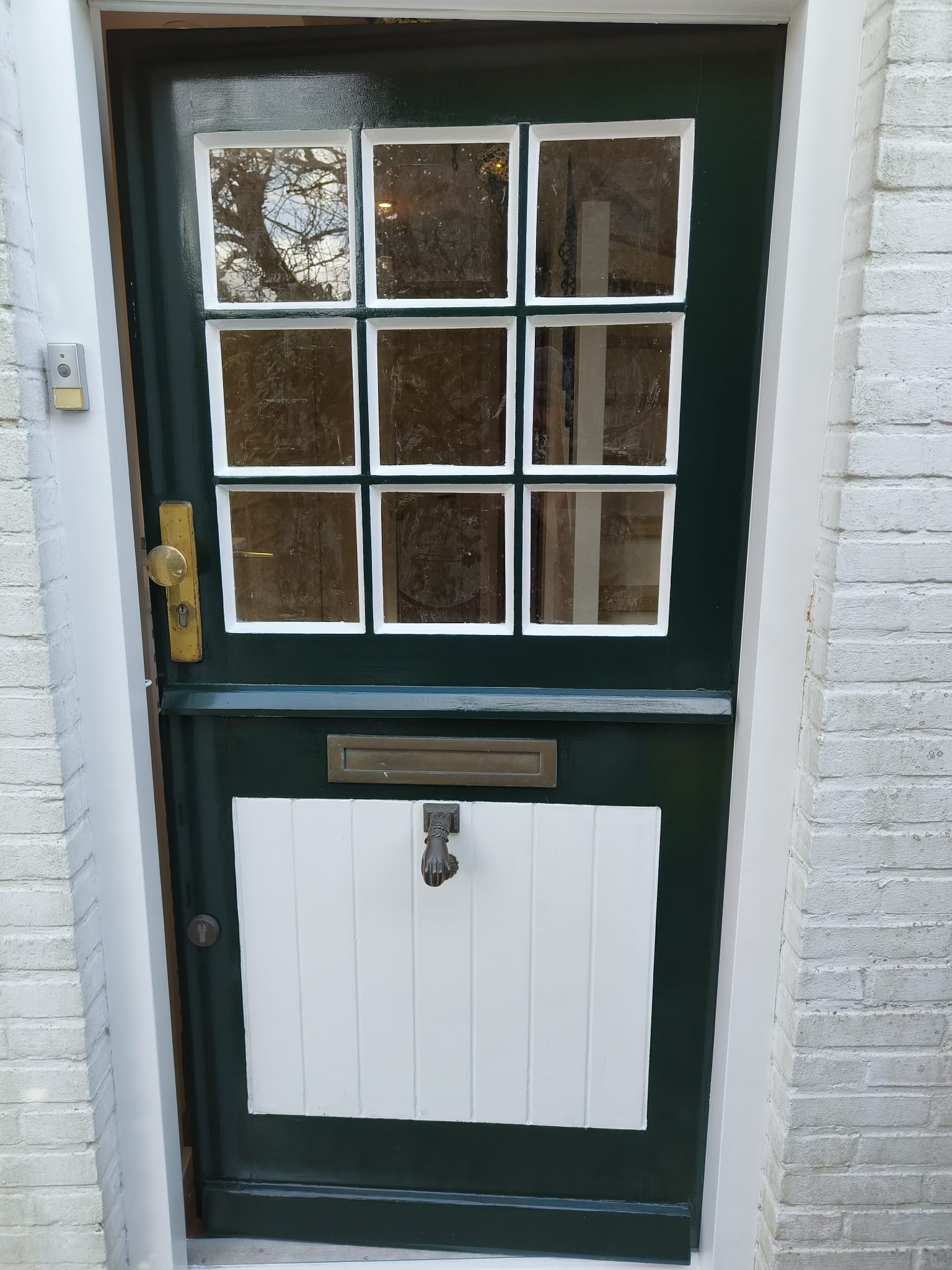 Donkergroene voordeur met witte glaslijsten en wit onderpaneel